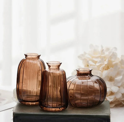 Three brown glass vases on a white surface with a blurred floral background