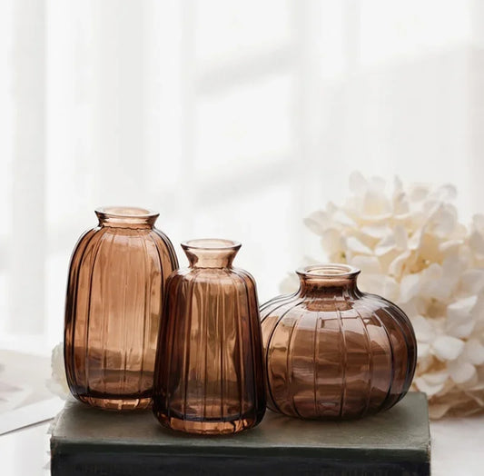 Three brown glass vases on a white surface with a blurred floral background